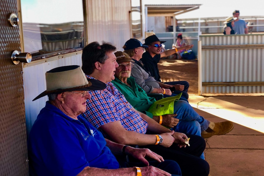 A group of men sitting under a verandah at the Meekatharra Races