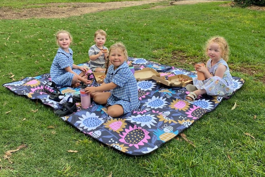 Four small children have a picnic on the grass.