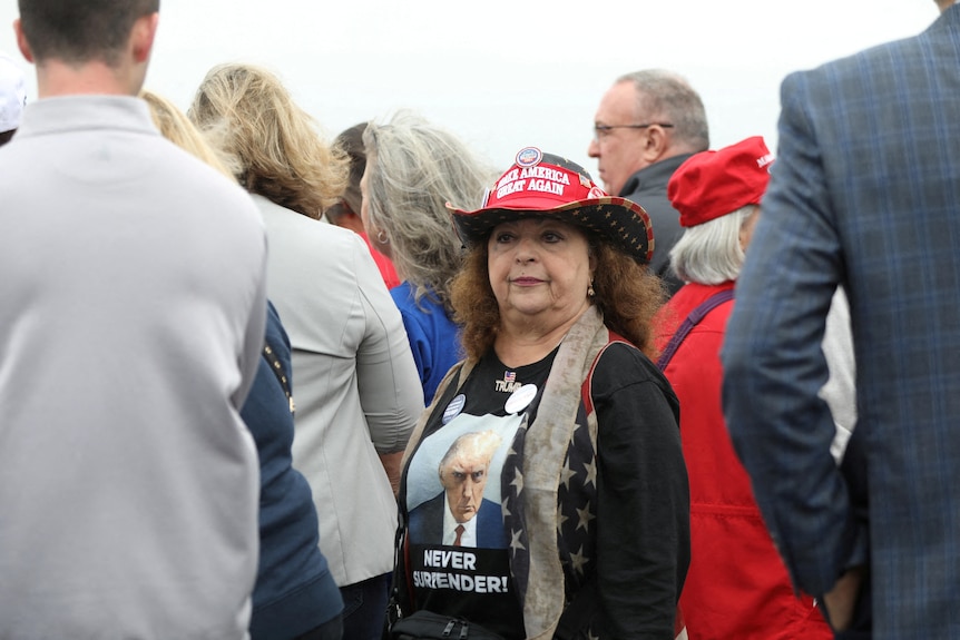 A woman wears a black shirt with the mug shot and the words 'never surrender' and a red MAGA cowgirl hat