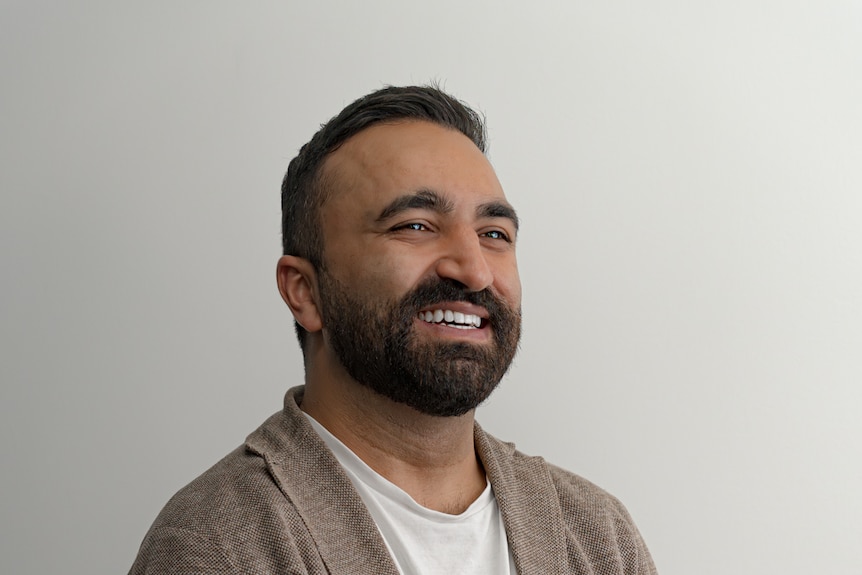 A man poses for a photo in front of a white wall