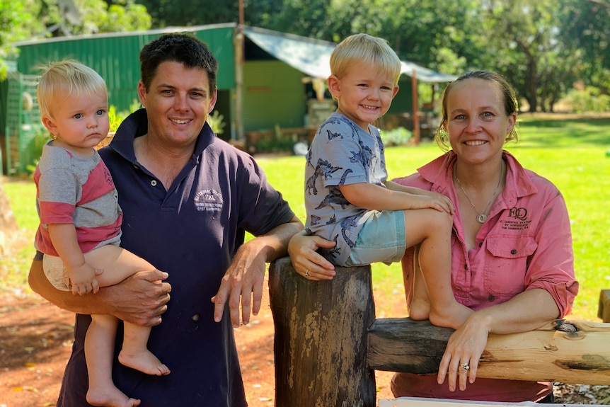 A man and his wife with their two boys leaning against a wooden gate