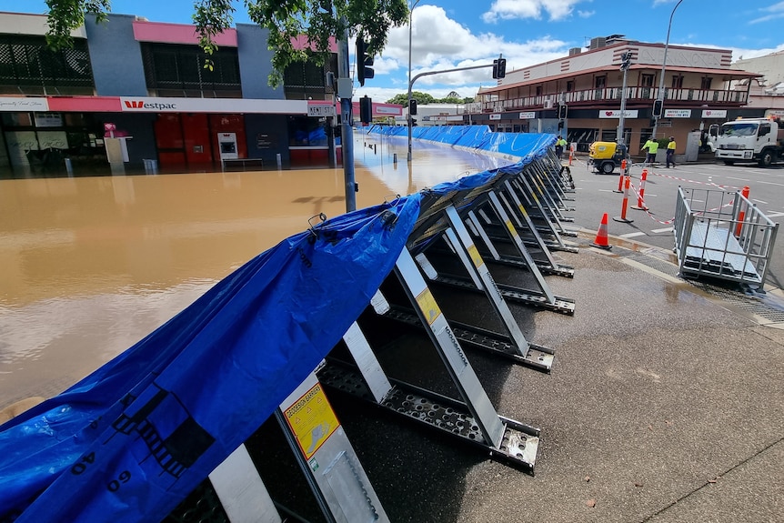 Flood water is being held back by a levee covered in blue tarp.