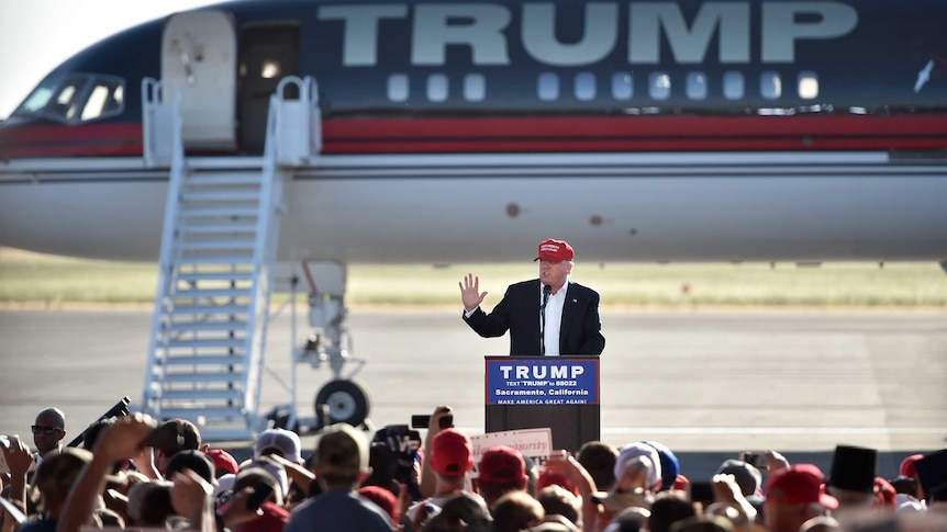 Donald Trump stands at a lectern in front of an aircraft bearing his name.