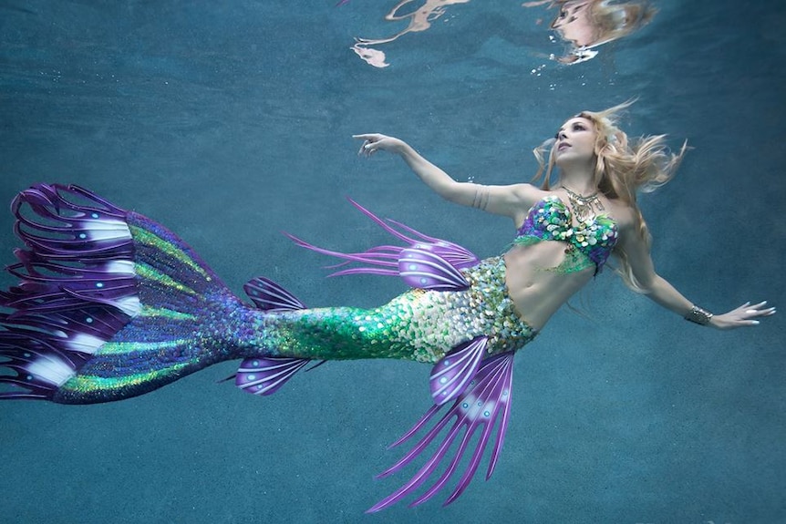 A woman swims under water in a blue and green mermaid costume.