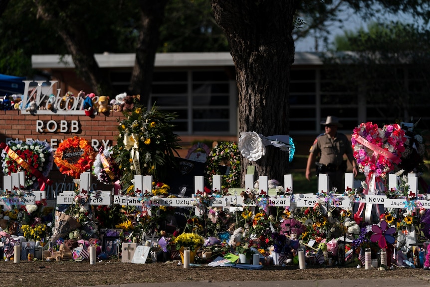 Flowers and candles are placed around crosses near a school sign.