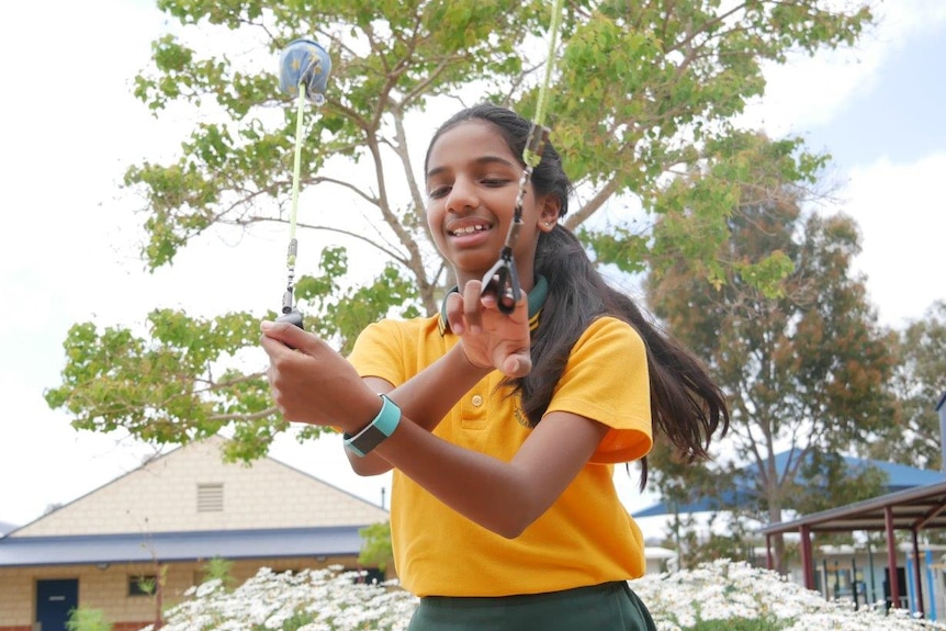 A young girl in a primary school court yard swinging circus equipment