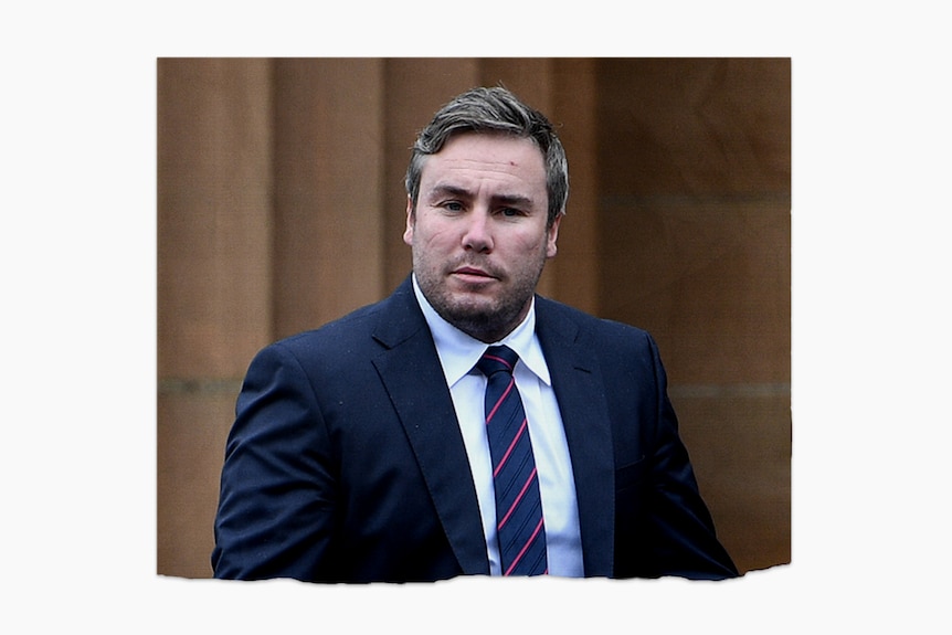 A man wearing a suit walks outside, turning to look at the camera.