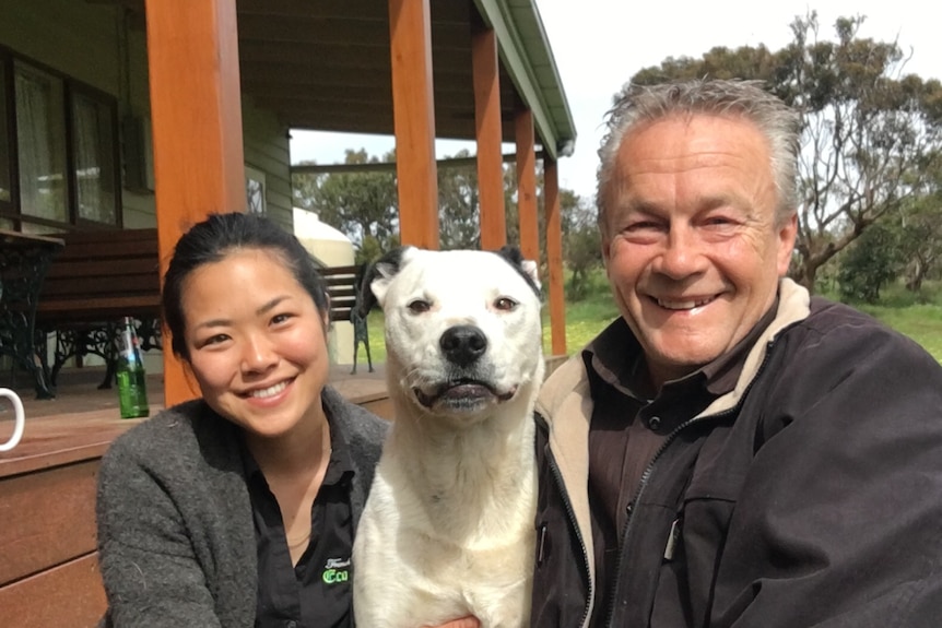 Man, woman and white and black dog sitting closely together and smiling outdoors.