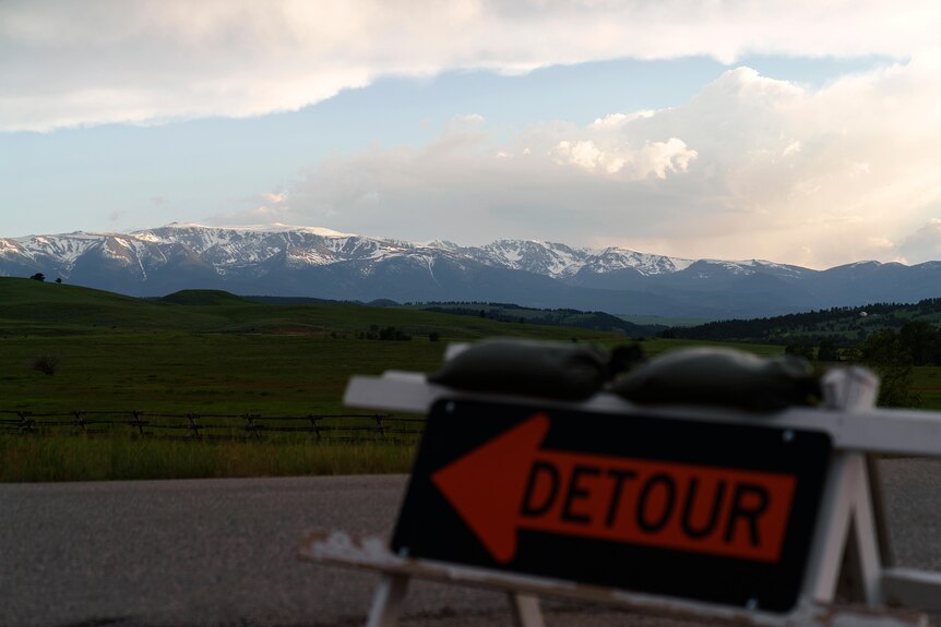 Snow capped mountains stand in the background, a detour sign blurred in the fore