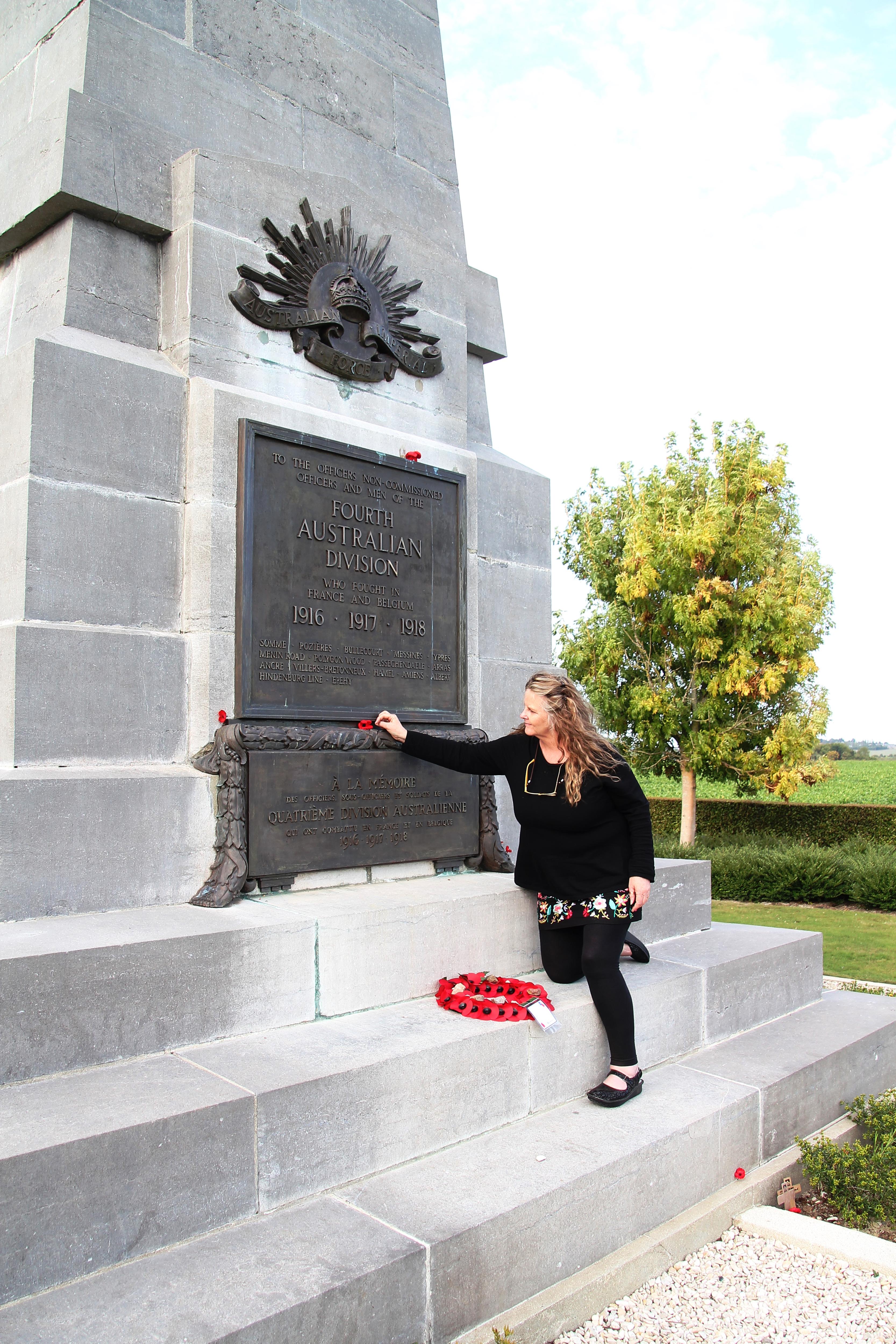 Lady with a black dress and long hair placing a poppy beneath the metal plate on a large cenotaph, 