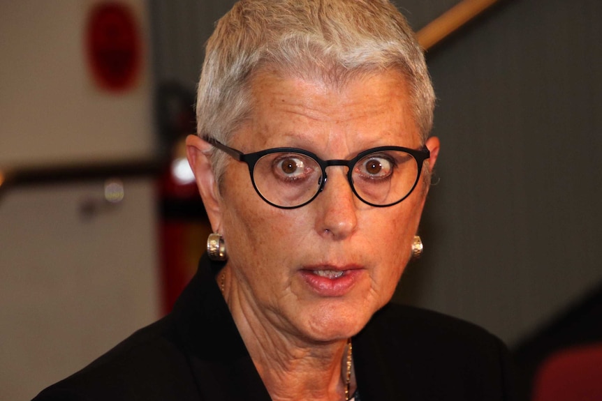 A close-up image of a woman with close cropped hair and glasses.