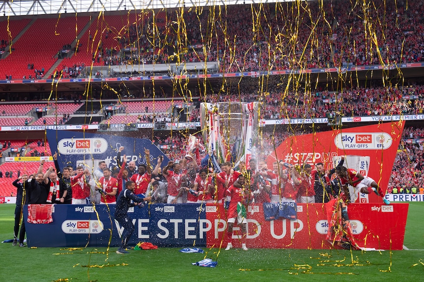 A men's soccer team wearing red and white celebrate after winning a trophy