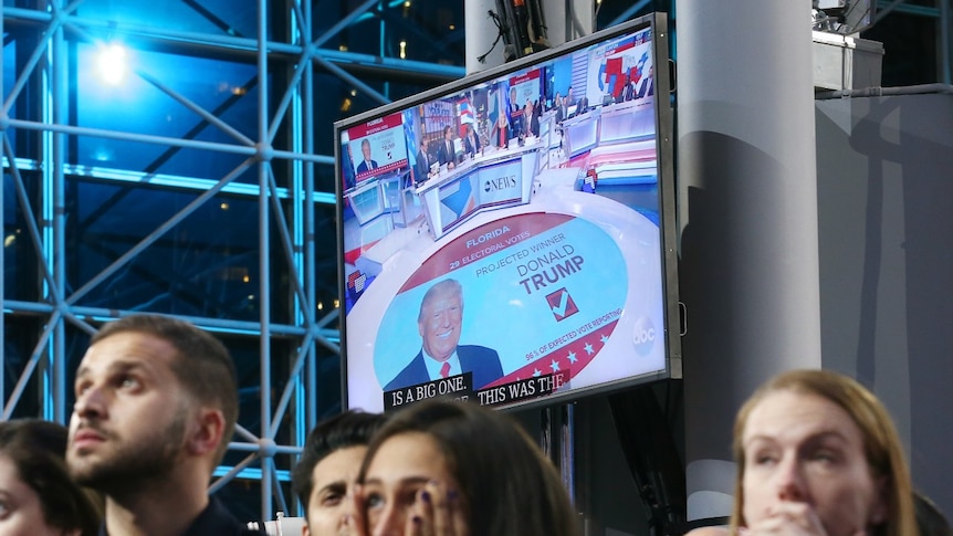 Supporters of Democratic presidential nominee Hillary Clinton watch and wait, with a Donald Trump image on a screen at rear