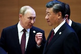 Vladimir Putin dressed in a suit and tie looks over at Xi Jinping dressed in a suit.