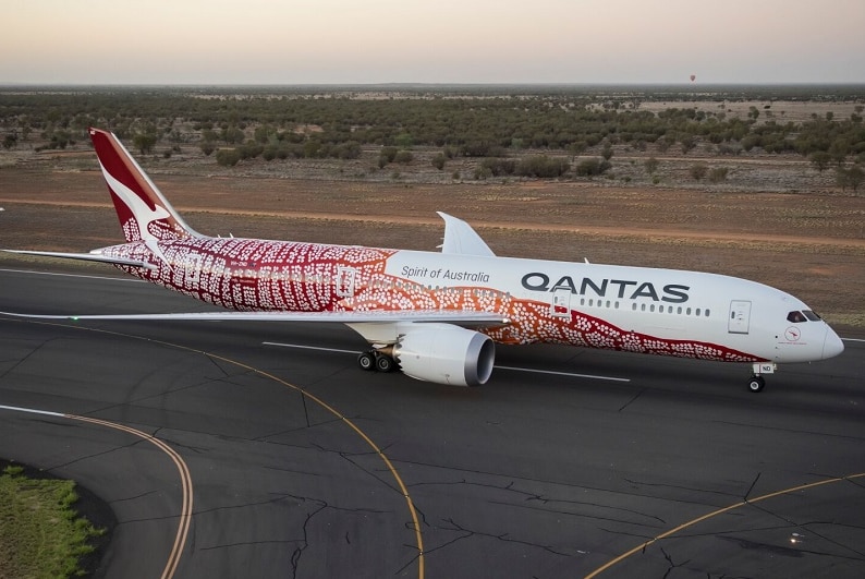 The Qantas Dreamliner featuring indigenous artwork, on the tarmac at Alice Springs at sunrise.