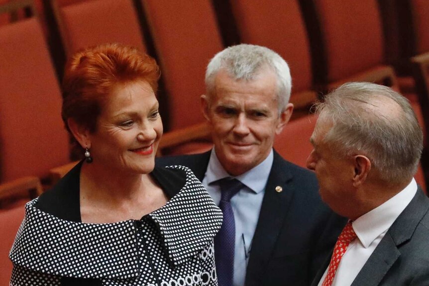 A red haired woman talks with two old white men in the Senate
