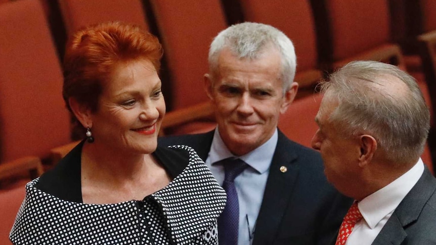 A red haired woman talks with two old white men in the Senate