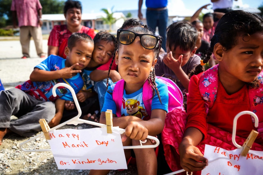 A schoolgirl holds a sign reading "Happy Manit Day" outside the school on Enetewak Island.