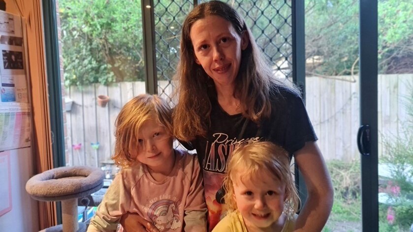 a woman with long hair wearing a dark t-shirt and her two young children.