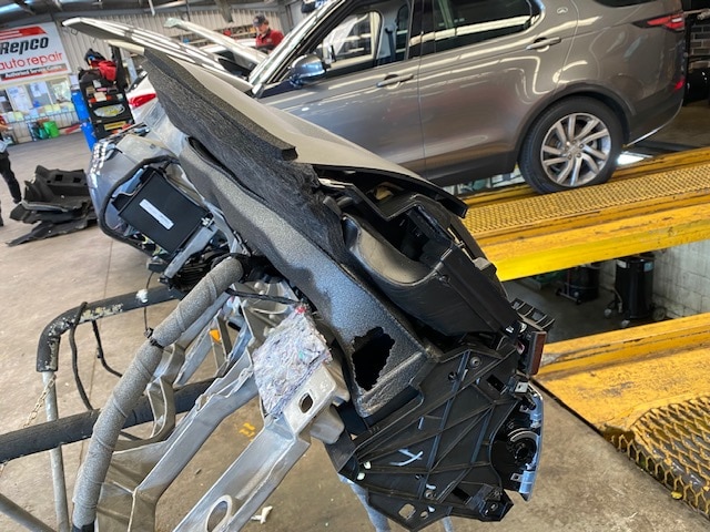 A mechanics shop, with an extracted dashboard sitting next to a car, with a large hole in its foam lining.