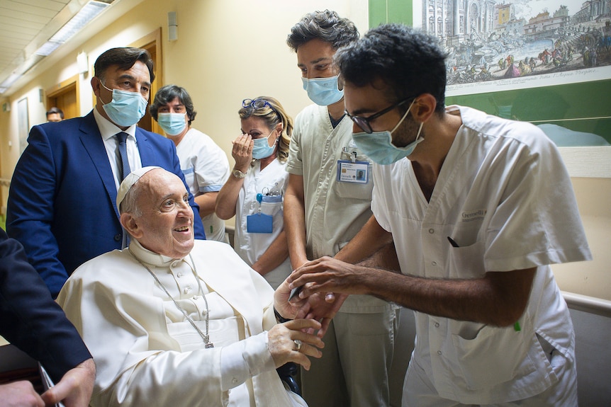 Pope Francis is greeted by hospital staff as he sits in a wheelchair .