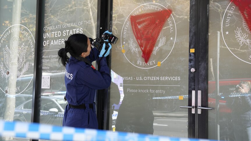 Police officers investigate a building with its windows smashed and doors spray-painted with red triangles
