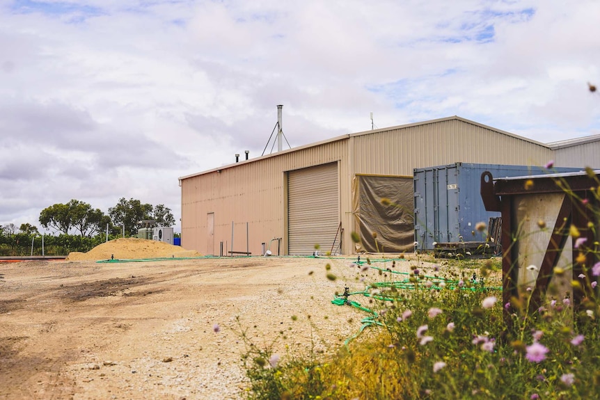 A large shed sits on a large patch of dirt next to some scaffolding marking a new building project.