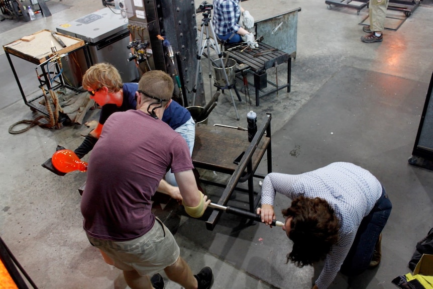 One person blows the glass while Catherine and another person assist.