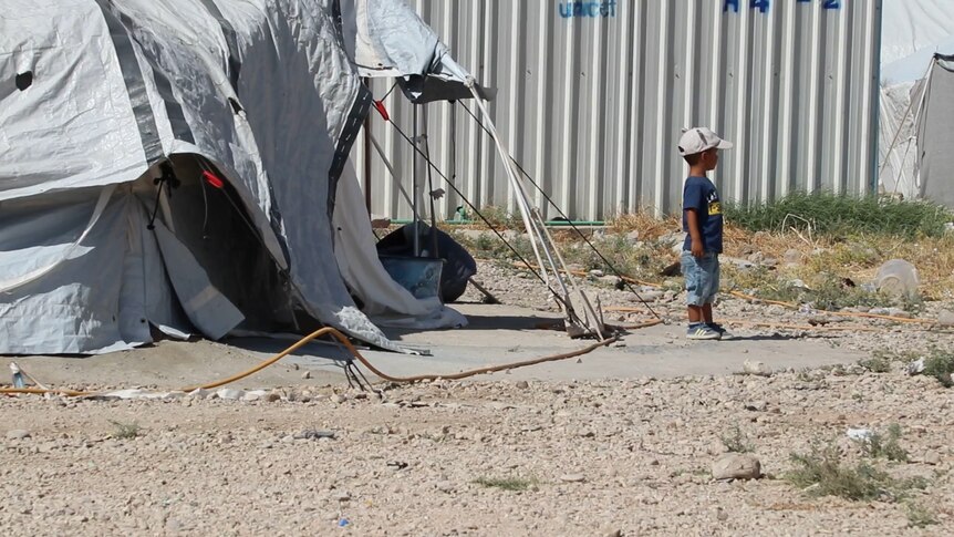 A small child stands outside a tent.