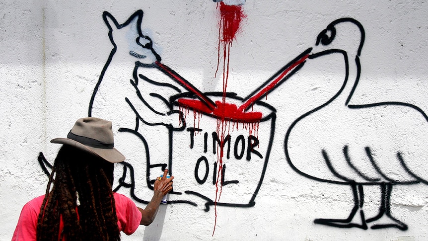 Graffiti artist painting Australian coat of arms animals sucking from a container marked Timor oil.