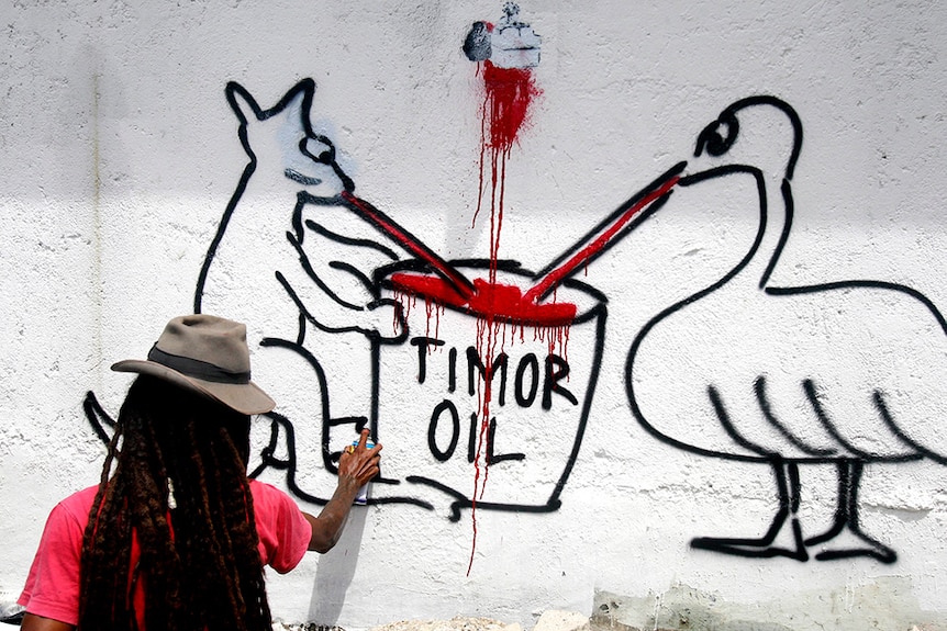 Graffiti artist painting Australian coat of arms animals sucking from a container marked Timor oil.