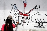 Graffiti artist painting Australian coat of arms animals sucking from a container marked Timor oil.