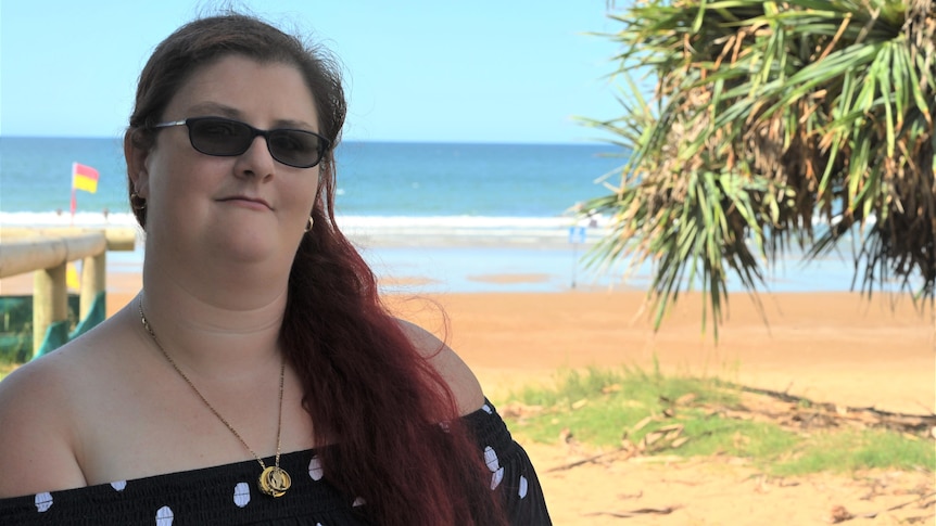 A woman with red hair sits in her wheelchair with the beach in the background.