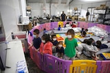 Children watch television from inside a playpen in an immigration detention facility