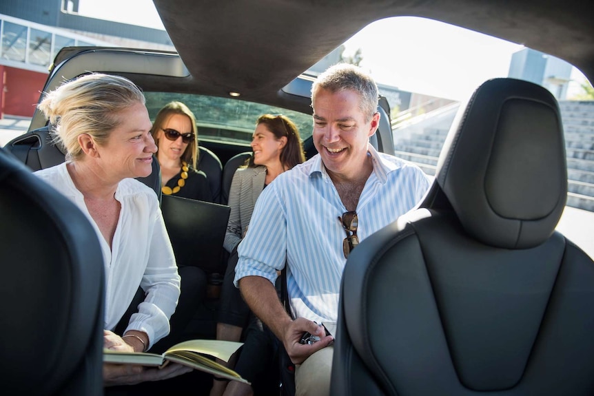 Four people sitting inside an electric vehicle ride sharing service as an alternative to running and owning their own cars.