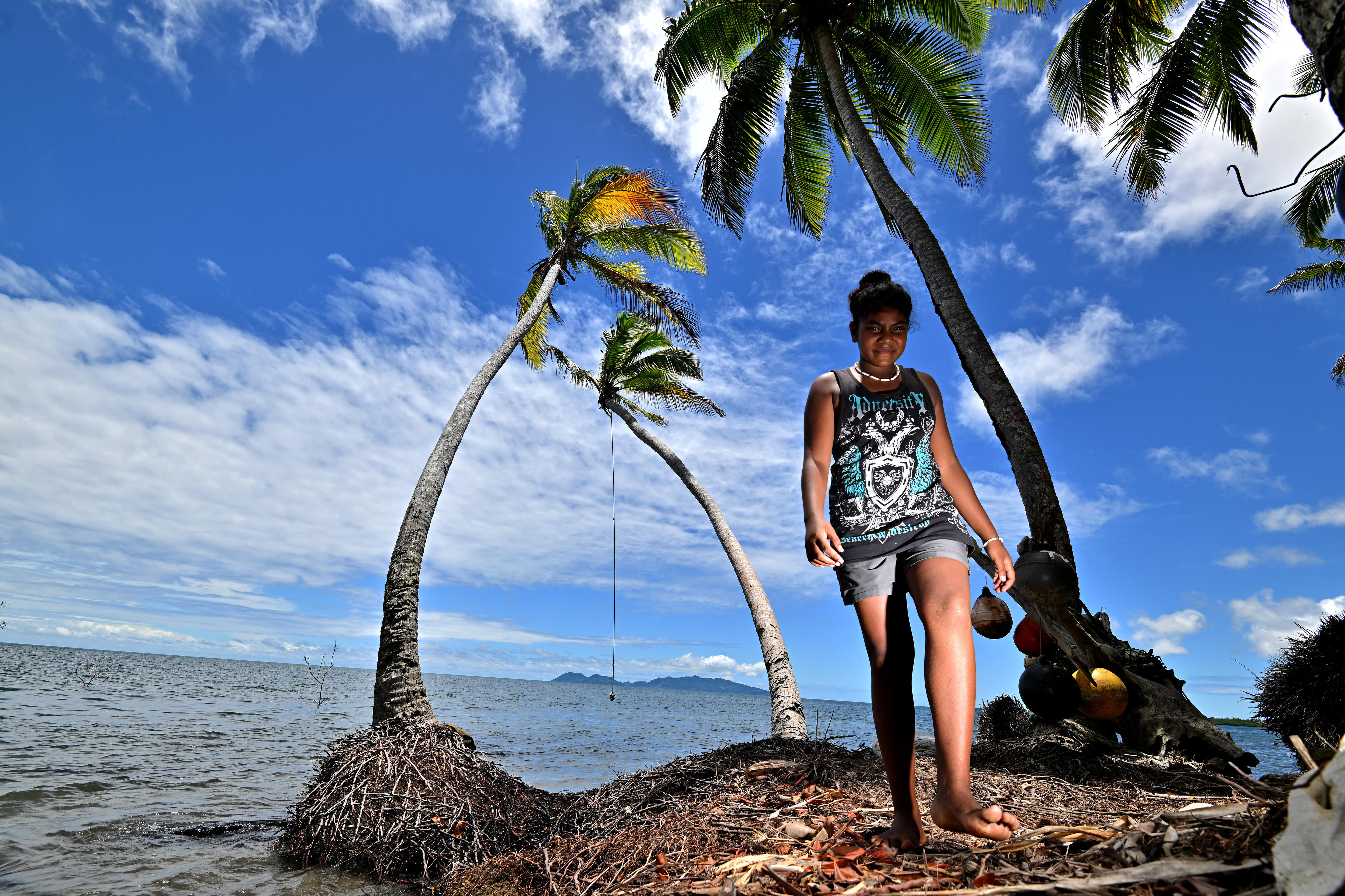 A young girl walks along the shore at high tide near coconut palms in Fiji