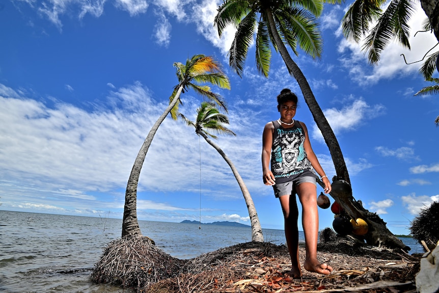 A young girl walks along the shore at high tide near coconut palms in Fiji
