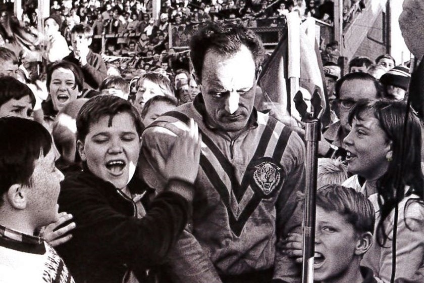 A black and white photograph of a rugby league player being swarmed by fans in celebration of their retirement
