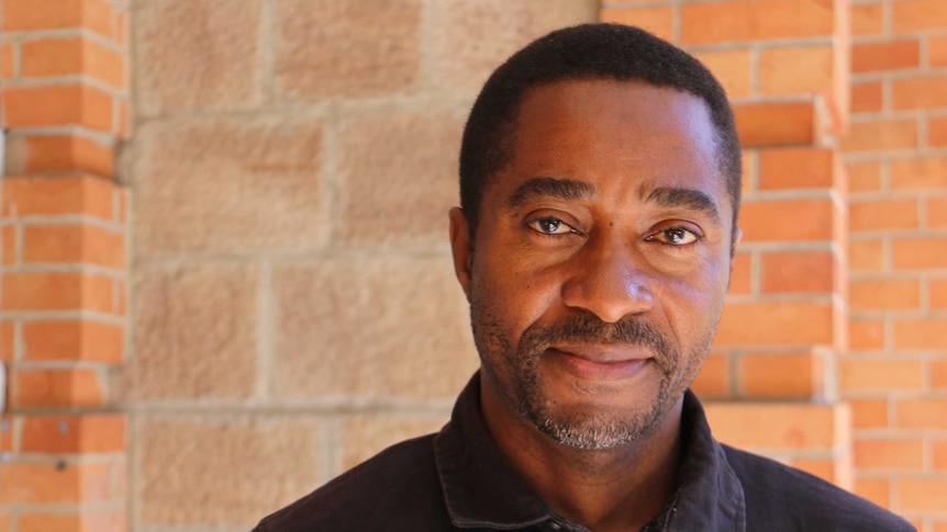 A man in front of a sandstone and red brick wall