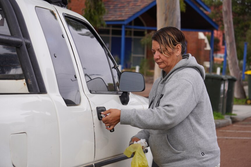 A woman unlocks the door of a white ute.