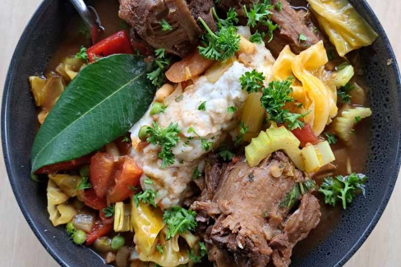Bowl of stew with meat, vegetables and a large lemon myrtle leaf