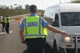 A police officer is flagging down a van at a  check point in WA.