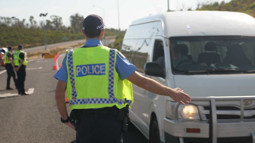 A police officer is flagging down a van at a  check point in WA.