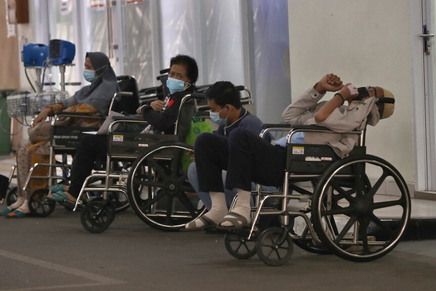 Several people sit in wheelchairs wearing masks while they wait for medical care