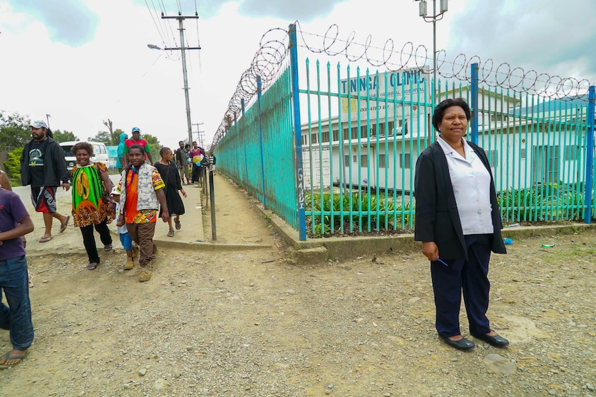 A woman looking strong and proud outside the blue gates to her clinic