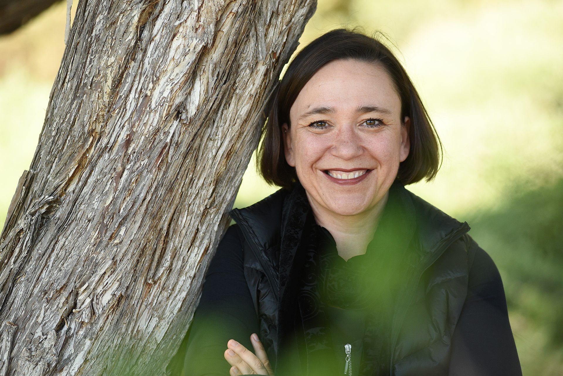 A woman smiles while next to a tree.