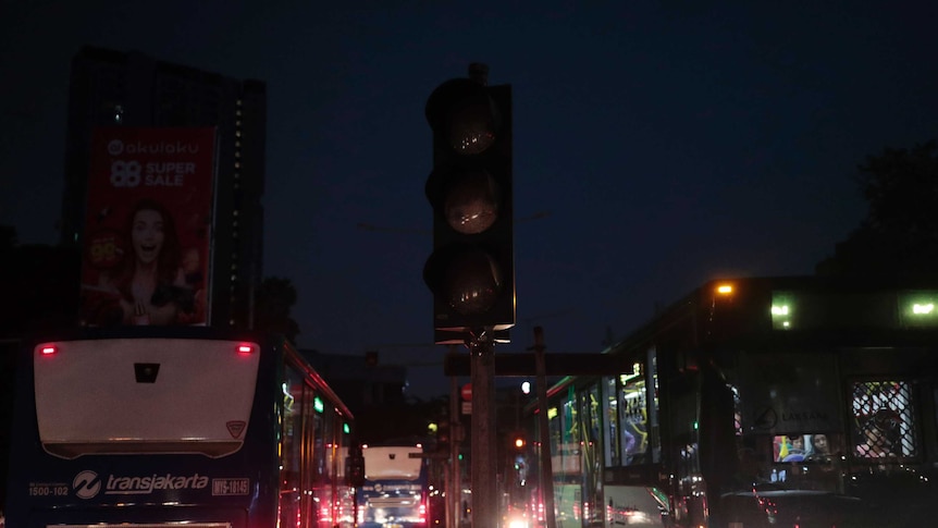 A traffic light is seen turned off during a power outage in Jakarta, Indonesia as various buses drive past it on either side.