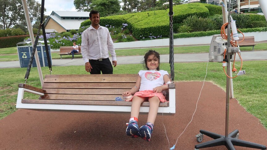 Alisha Kapoor sits on a swing while dad Raj Kapoor stands behind.