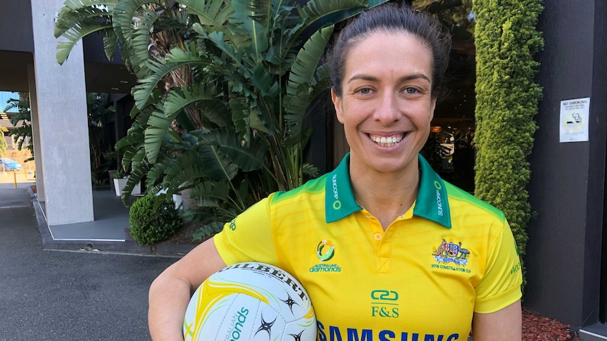 A netballer poses in her national team gear while holding a ball.