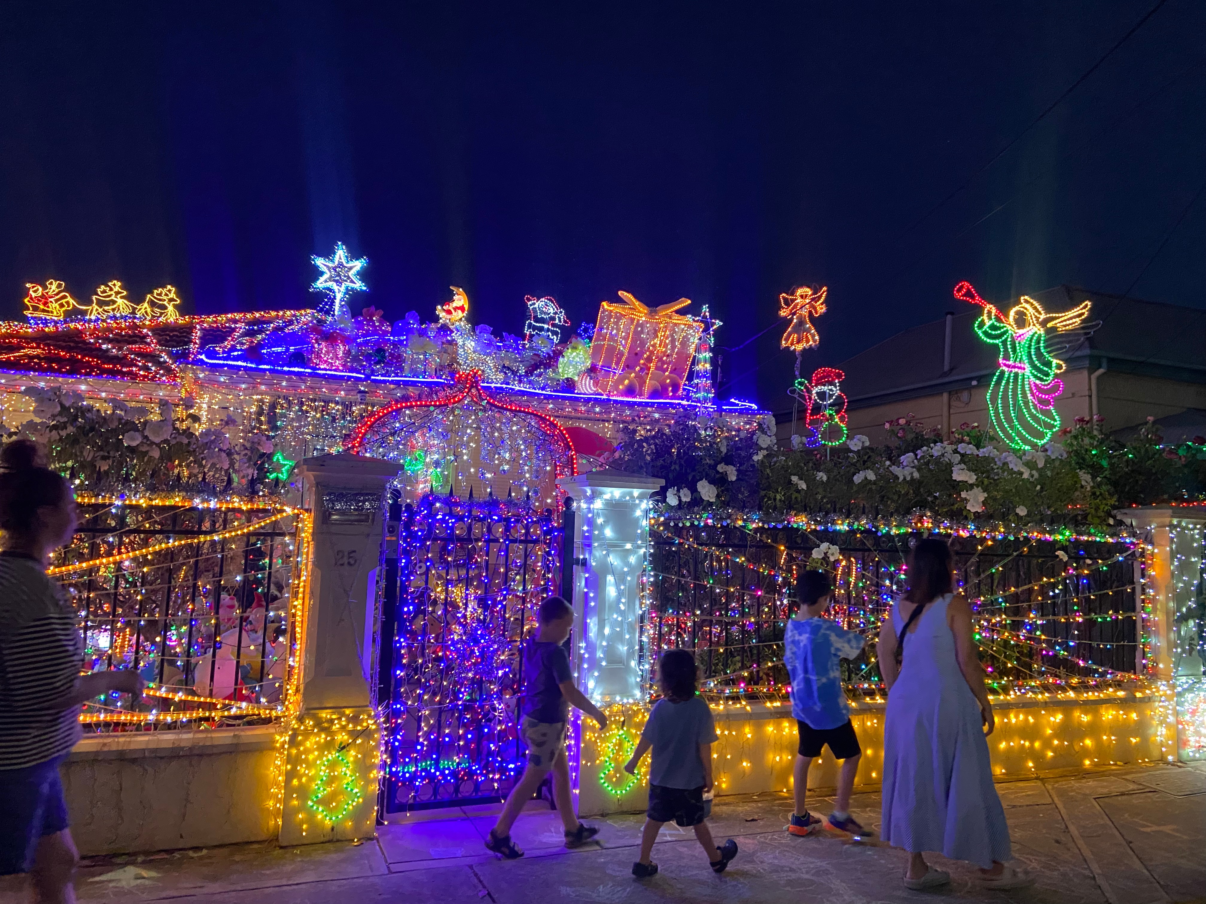 Crianças passando por uma casa com elaboradas decorações natalinas.